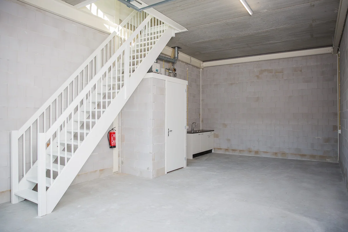 Lege bedrijfsruimte aan de Laan van ’s-Gravenmade met een witte trap, bergkast, keukenblok en betonnen vloer.